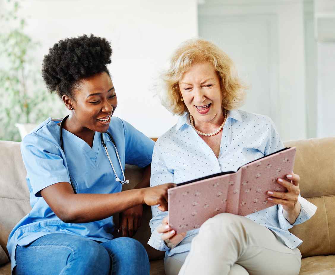 Doctor or nurse caregiver with senior woman looking at photo album and picture or book or brochure at home or nursing home