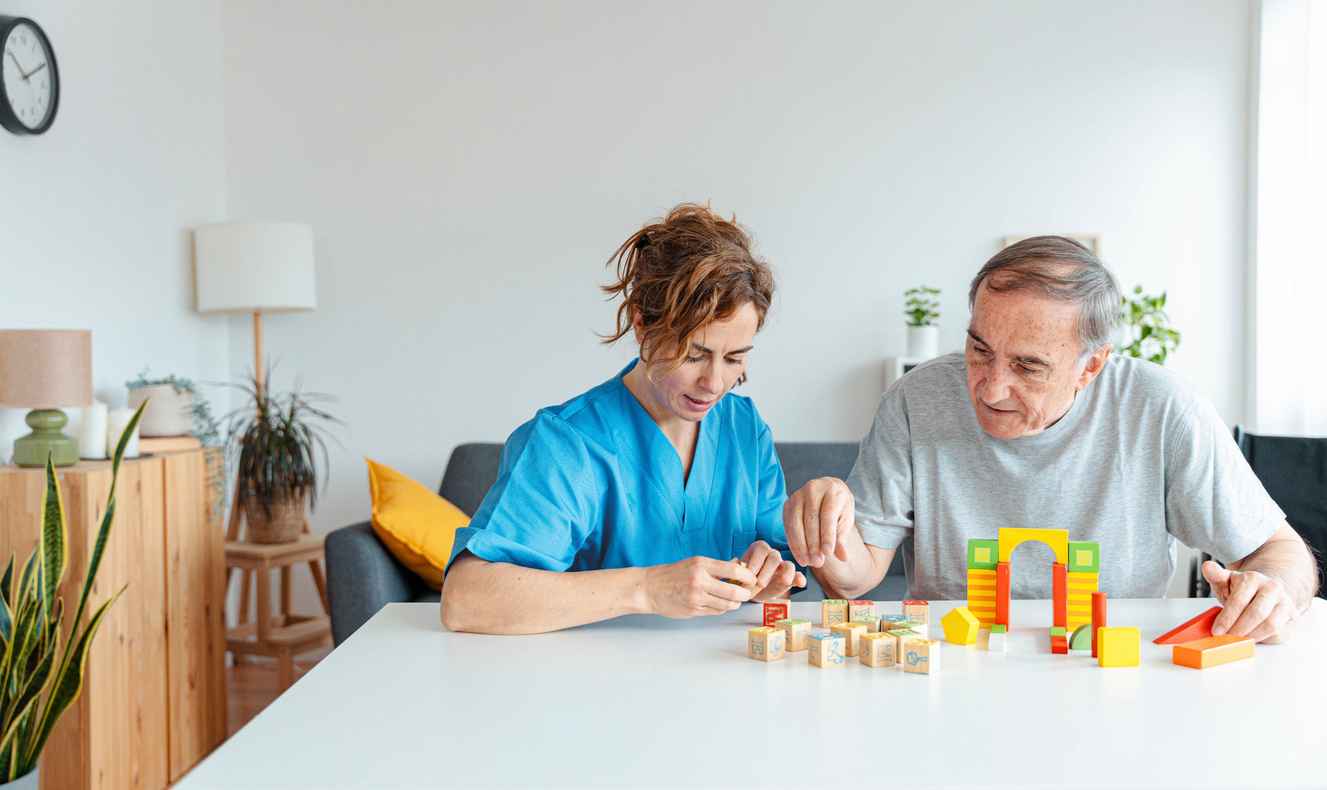 Professional nurse caregiver in geriatric clinic helps senior man with Alzheimer's disease - Old patient playing puzzle in retirement home - Healthcare and medical concept