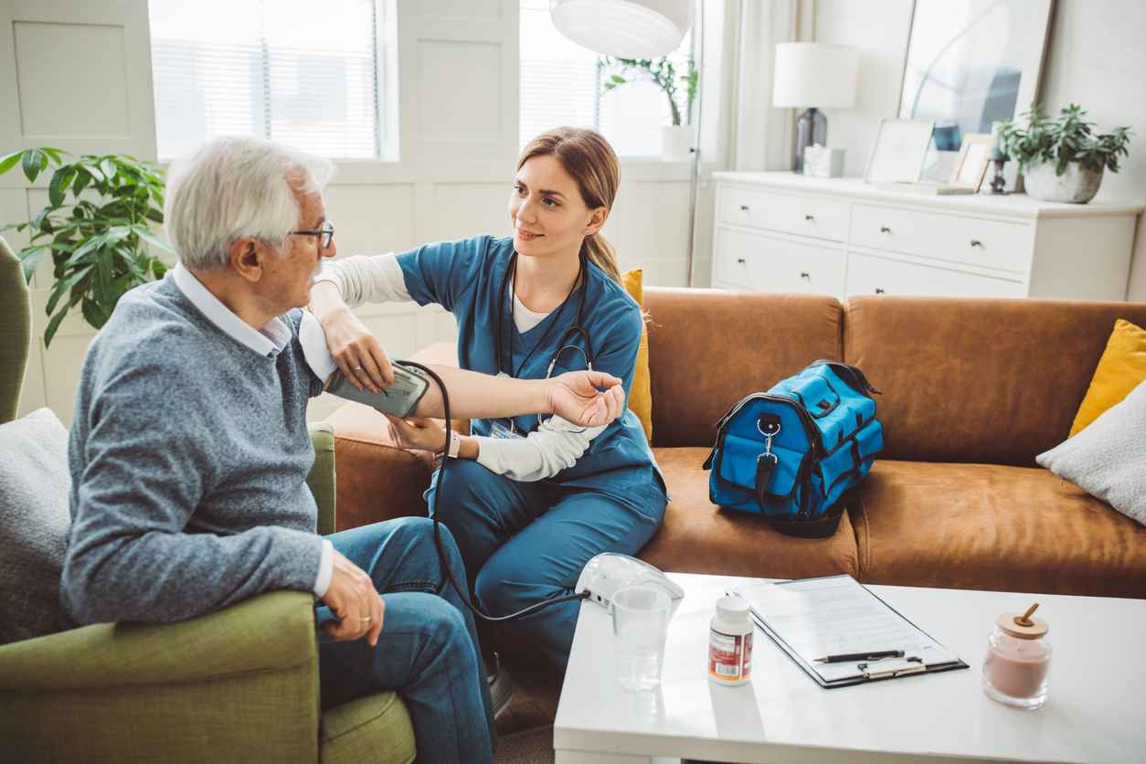 Nurse visiting mature patient at home. She is measuring blood pressure to patient at his living room.
